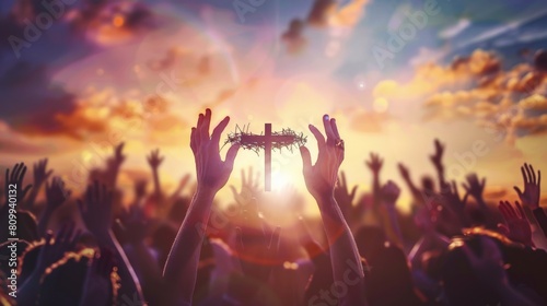 Hands holding a cross with a crown of thorns in front of a crowd with the sun in the background