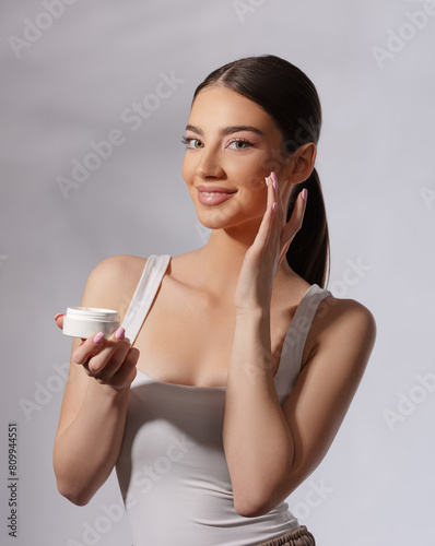 Beautiful woman on bright gray background holding a crème. Beauty portrait.