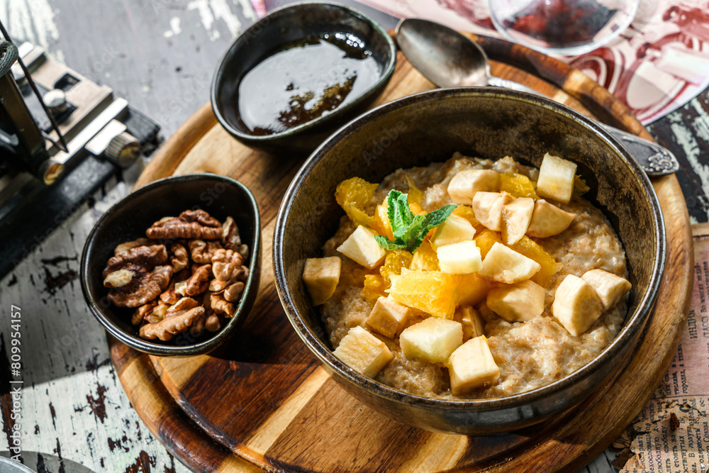 Oatmeal porridge with pieces of fruit, nuts and honey in bowl on wooden background. Healthy breakfast, top view Oatmeal porridge with pieces of fruit, nuts and honey in bowl on wooden background. Healthy breakfast, top view