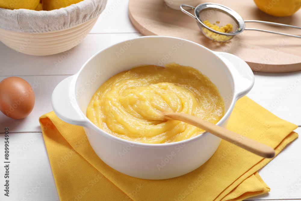 Delicious lemon curd in bowl, ingredients, spoon and sieve on white wooden table, closeup Delicious lemon curd in bowl, ingredients, spoon and sieve on white wooden table, closeup