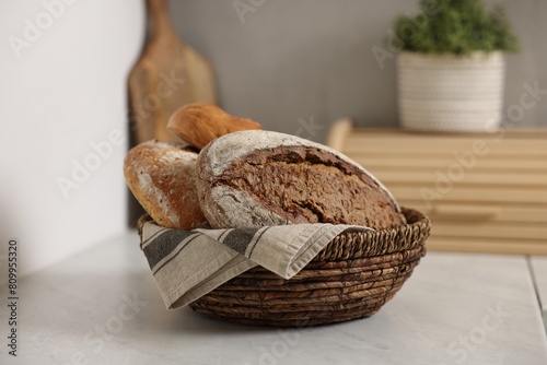 Wicker bread basket with freshly baked loaves on white marble table in kitchen photo