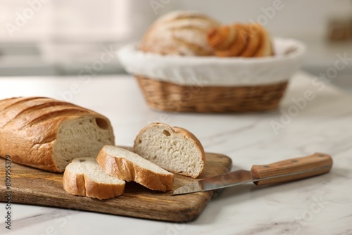 Wicker bread basket with freshly baked loaves and knife on white marble table in kitchen
