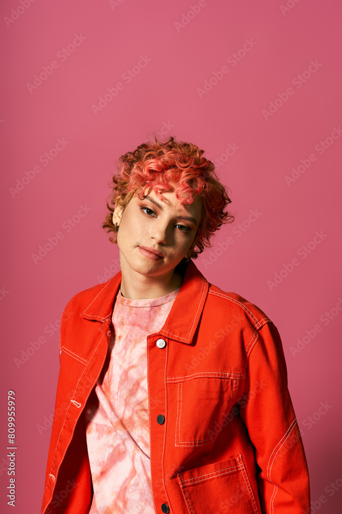 A captivating woman with red hair stands elegantly before a pink wall. A captivating woman with red hair stands elegantly before a pink wall.