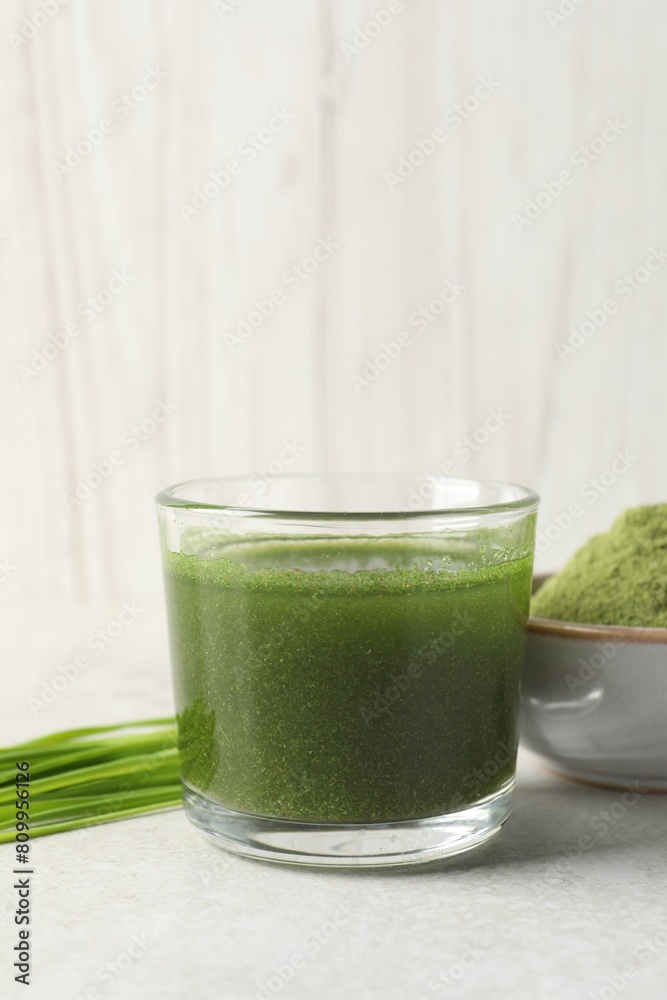 Wheat grass drink in glass, fresh sprouts and bowl of green powder on light table