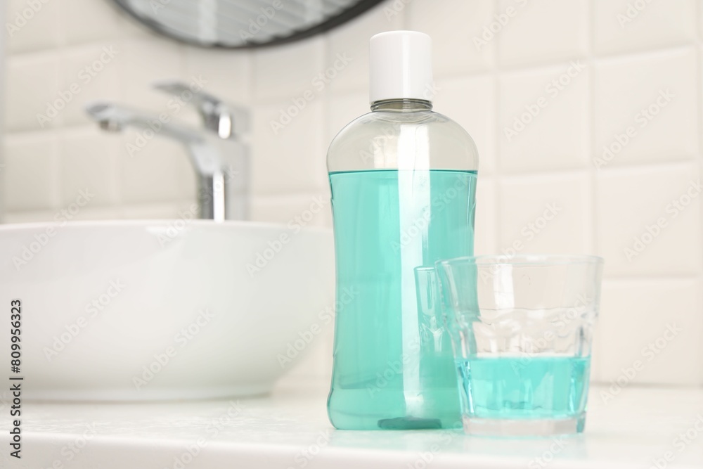Bottle of mouthwash and glass on white table in bathroom, space for text Bottle of mouthwash and glass on white table in bathroom, space for text