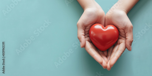 Woman hands holding red heart on solid light blue background. Health care, organ donation, cardiac health problems. photo