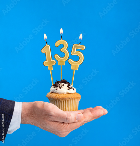 Hand delivering birthday cupcake - Candle number 135 on blue background