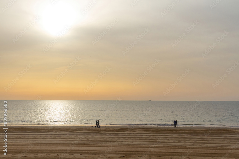 Beach with silhouettes of a few people walking along the sea, with the sand recently cleaned and the sun in the sky with sunset tones, Chipiona Beach, Cádiz, Andalusia, Spain 