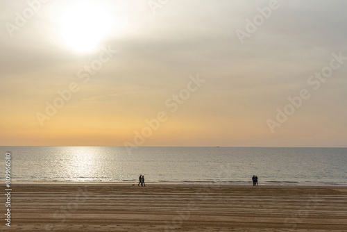 Beach with silhouettes of a few people walking along the sea, with the sand recently cleaned and the sun in the sky with sunset tones, Chipiona Beach, Cádiz, Andalusia, Spain 