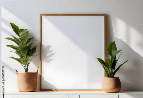 A white wall with a framed poster and a potted plant in front of a window with sunlight streaming in