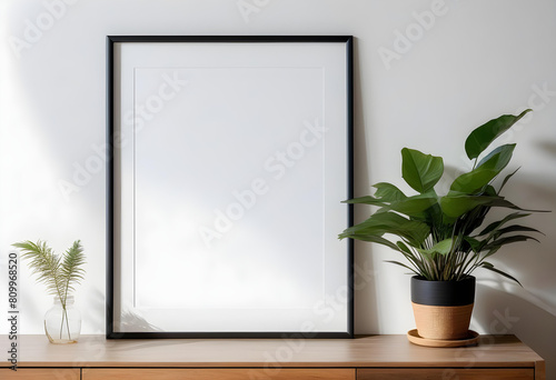 A white wall with a minimalist frame mockup poster and a potted plant in Sunlight streams through the window.