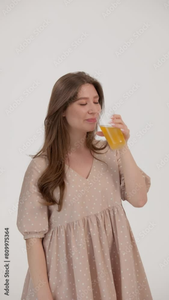 Vertical. Young pregnant woman drinks juice. Her husband approaches her and hugs his wife by the waist. Both are smiling and looking at the camera. The concept of healthy eating in a young family. Vertical. Young pregnant woman drinks juice. Her husband approaches her and hugs his wife by the waist. Both are smiling and looking at the camera. The concept of healthy eating in a young family.