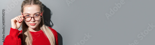 Portrait of a beautiful blonde woman wearing glasses with copy space for textspace on a gray background. A pretty girl with glasses and a red blouse in the studio. Use for a banner. photo