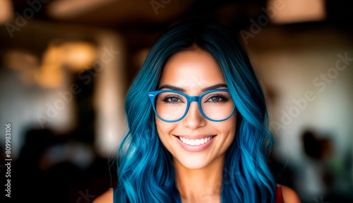 A woman with blue hair and glasses smiles at the camera.