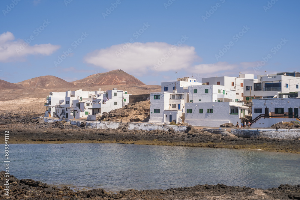 Bay and typical houses of the fishing village of Caleta de Caballo. White houses. Rock coast in the foreground. Turquoise water. Calm sea. Caleta de Caballo, Lanzarote, Canary Islands, Spain Bay and typical houses of the fishing village of Caleta de Caballo. White houses. Rock coast in the foreground. Turquoise water. Calm sea. Caleta de Caballo, Lanzarote, Canary Islands, Spain