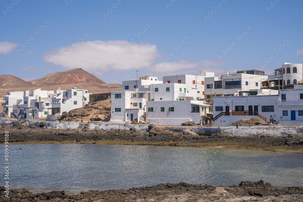 Bay and typical houses of the fishing village of Caleta de Caballo. White houses. Rock coast in the foreground. Turquoise water. Calm sea. Caleta de Caballo, Lanzarote, Canary Islands, Spain