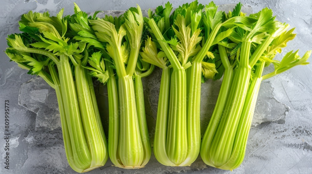 A collection of celery stalks aligned on a table, with one atop a sheet of paper A collection of celery stalks aligned on a table, with one atop a sheet of paper