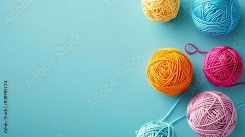   A collection of balls of yarn aligned next to one another on a blue surface Nearby, two crochet hooks rest photo