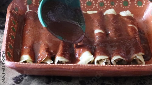 Slow motion still shot of spoon pouring mole sauce on tacos enchiladas. enmoladas mexican food