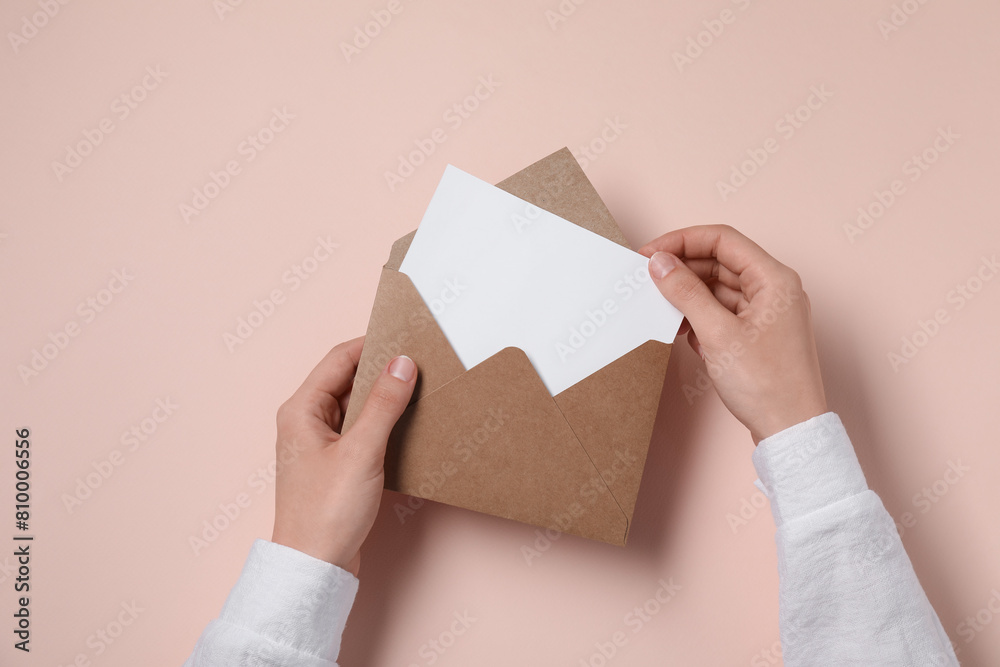 Woman taking card out of letter envelope at beige table, top view Woman taking card out of letter envelope at beige table, top view
