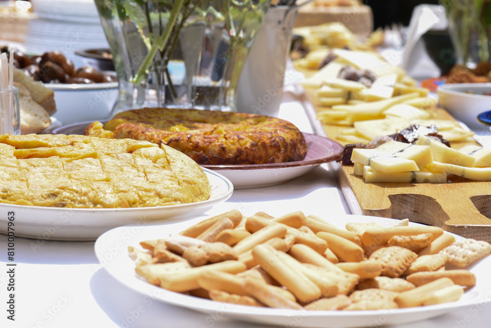 square table with food for a popular aperitif at a village festival. potato omelette, cheeses, sausages, croquettes on wooden boards and plates, vases with natural roses. square table with food for a popular aperitif at a village festival. potato omelette, cheeses, sausages, croquettes on wooden boards and plates, vases with natural roses.