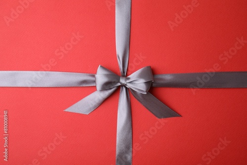 Grey satin ribbon with bow on red background, top view