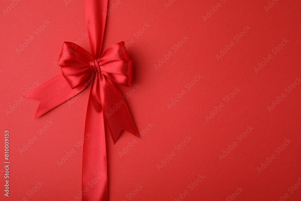 Bright satin ribbon with bow on red background, top view. Space for text