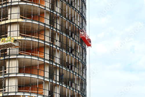 Workers on construction cradle prepare building for structural glazing. Suspended platform, construction craddle hanging on building. Glazing of high-rise building