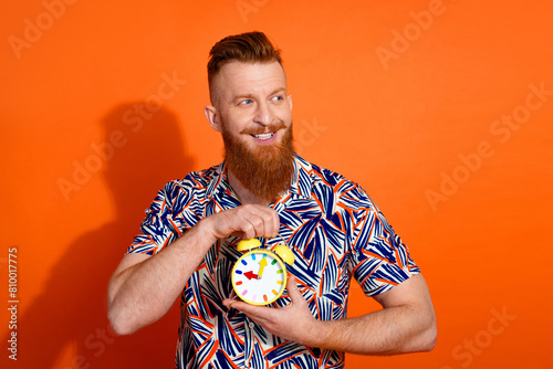 Photo of dreamy positive guy dressed print shirt holding clock lookng emtpy space isolated orange color background photo