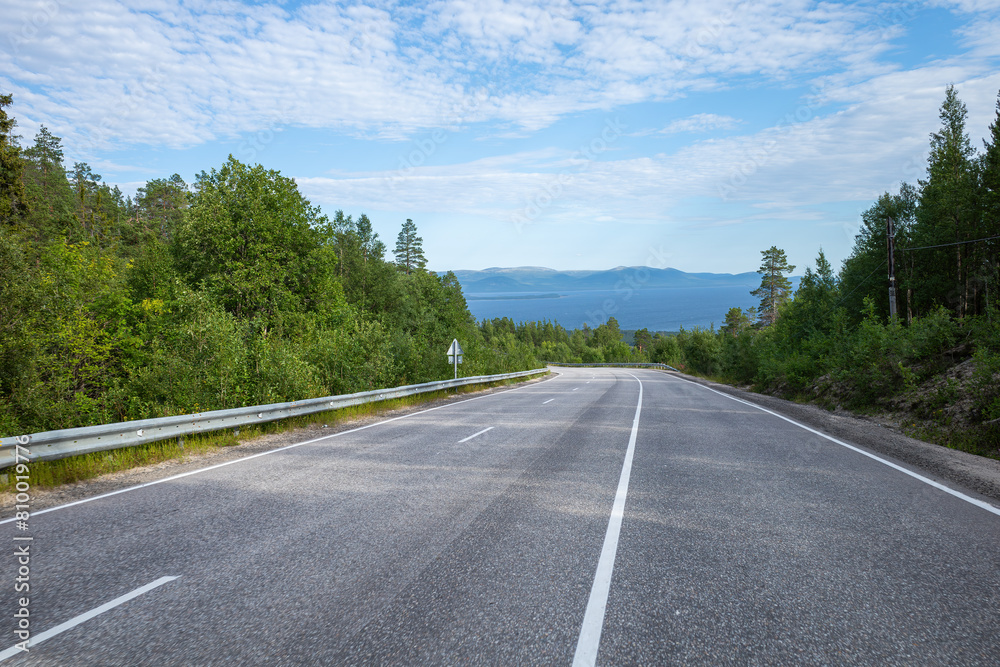 summer panoramic view of the highway among the hills with forest on the background of the sea and blue sky with clouds