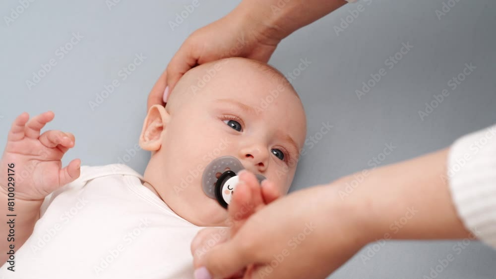 Cute baby lies in crib with pacifier, mom strokes baby on head, putting him to sleep, close-up. Healthy sleep for newborn baby crib. Concept of maternity leave, childcare, infancy. Cute baby lies in crib with pacifier, mom strokes baby on head, putting him to sleep, close-up. Healthy sleep for newborn baby crib. Concept of maternity leave, childcare, infancy.