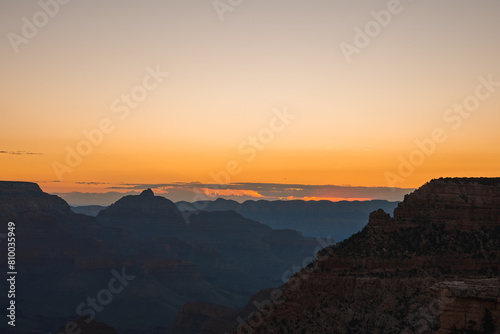 Serene sunset view over a rugged canyon landscape with warm orange hues fading into blue skies. Reminiscent of Grand Canyon, Arizona, USA. Peaceful and contemplative.