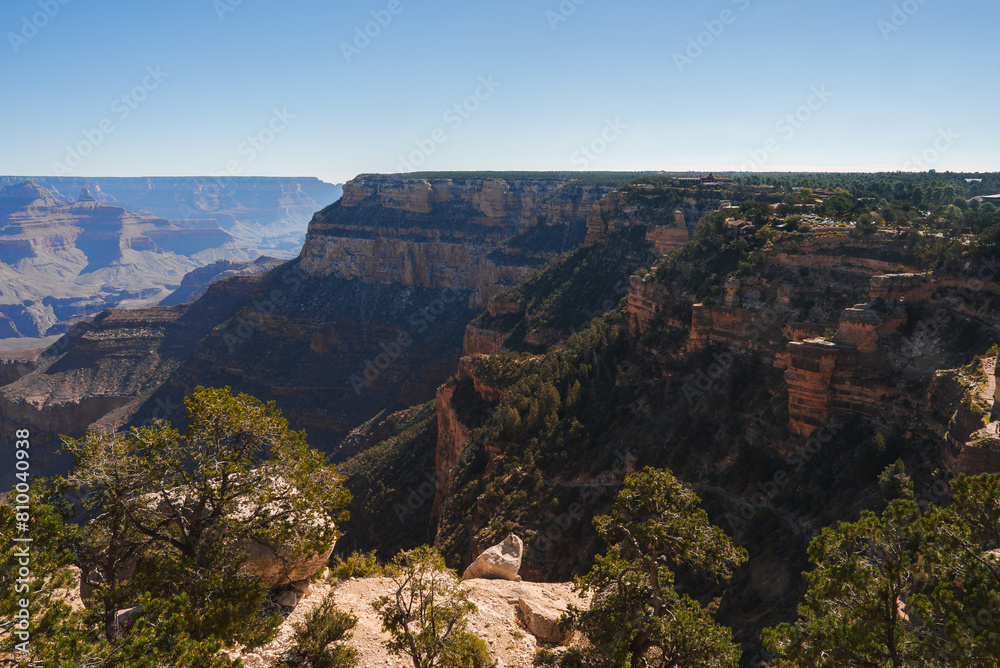 Explore breathtaking panoramic view of Grand Canyon under clear blue skies. Vast geological landscape showcases red and brown rock formations in Arizona, USA.