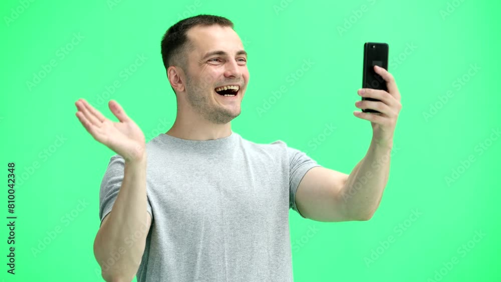 A man in a gray T-shirt, on a green background, close-up, with a phone A man in a gray T-shirt, on a green background, close-up, with a phone