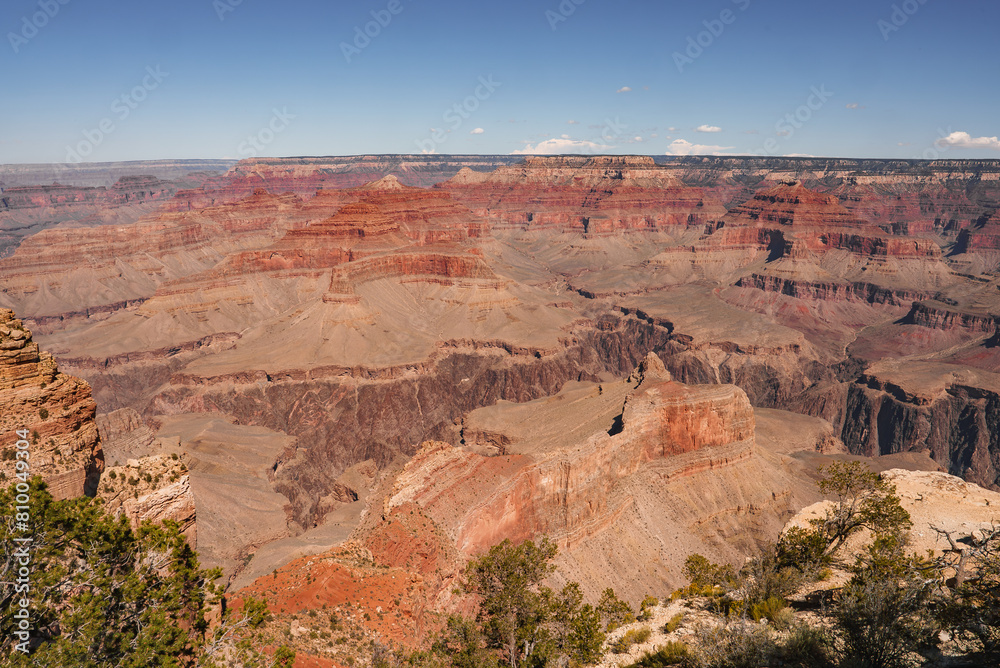 Expansive view of Grand Canyon, Arizona, USA, showcases stunning red rock layers, clear sky, deep gorges, rugged terrain. No people visible, untouched beauty captured.