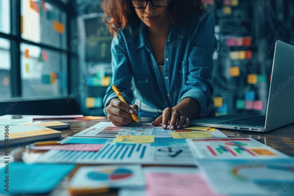 A woman in a blue shirt is working on a project with sticky notes and a laptop.