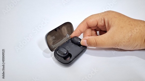 a hand holding black earbuds on a plain white background. 