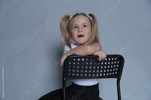 Smiling girl with pigtails leaning on a black chair, exuding confidence and comfort in her own skin, posing for a portrait.
