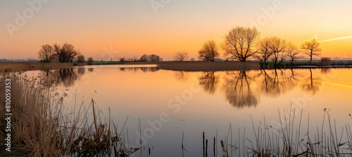 A sunset scene in a polder  where the sky is painted in hues of orange and pink above a mirror-like water surface reflecting the calmness