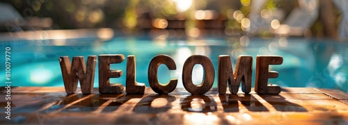The word WELCOME made of wooden letters on the table by the poolside, summer background with a blurred swimming pool and sunlight effect
