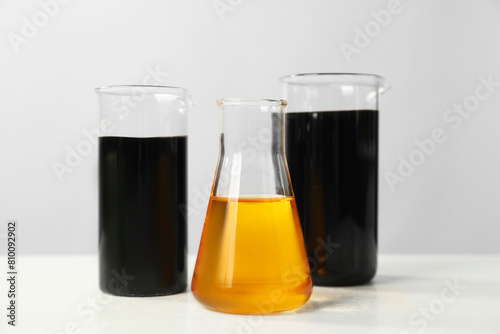 Beakers and flask with different types of oil on white table photo