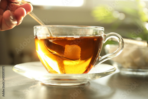 Woman adding sugar into cup of tea at table, closeup