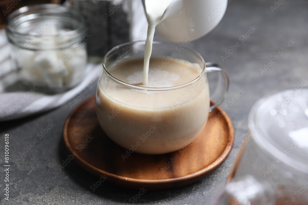 Pouring milk into cup of tea on grey table, closeup Pouring milk into cup of tea on grey table, closeup
