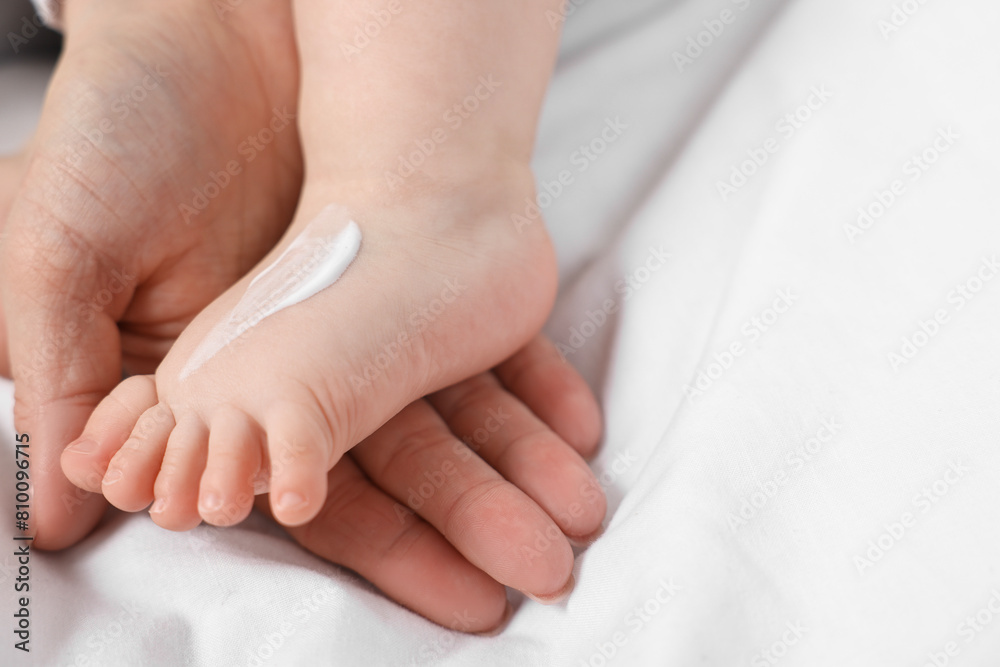 Woman applying body cream onto baby`s foot on bed, closeup Woman applying body cream onto baby`s foot on bed, closeup