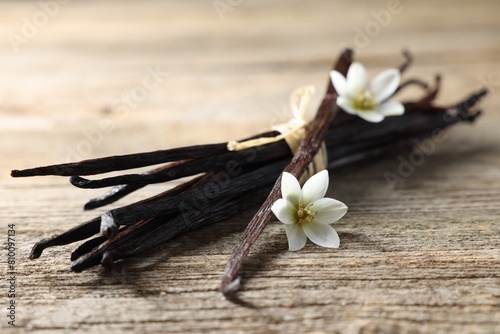 Bunch of vanilla pods and flowers on wooden table, closeup