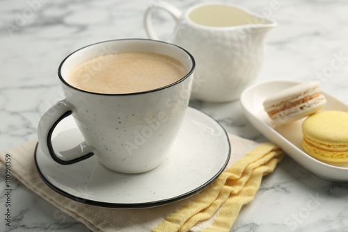 Tasty cappuccino in cup, macarons and saucer on white marble table, closeup