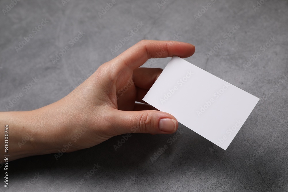 Woman holding blank card at grey table, closeup. Mockup for design Woman holding blank card at grey table, closeup. Mockup for design