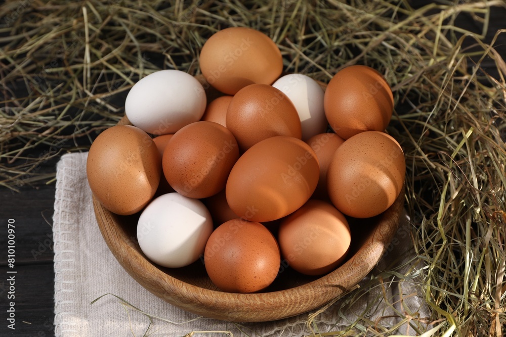 Fresh chicken eggs in bowl and dried hay on black wooden table Fresh chicken eggs in bowl and dried hay on black wooden table