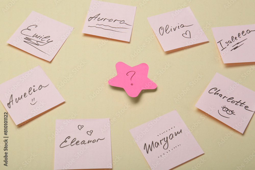 Choosing baby name. Paper stickers with different names and question mark on beige background Choosing baby name. Paper stickers with different names and question mark on beige background