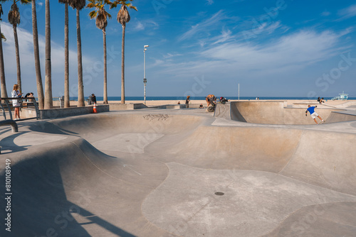 Experience the vibrant Venice Beach Skatepark in Los Angeles, California under sunny skies. Skaters of all levels enjoy the smooth ramps and bowls with a backdrop of iconic palm trees. photo